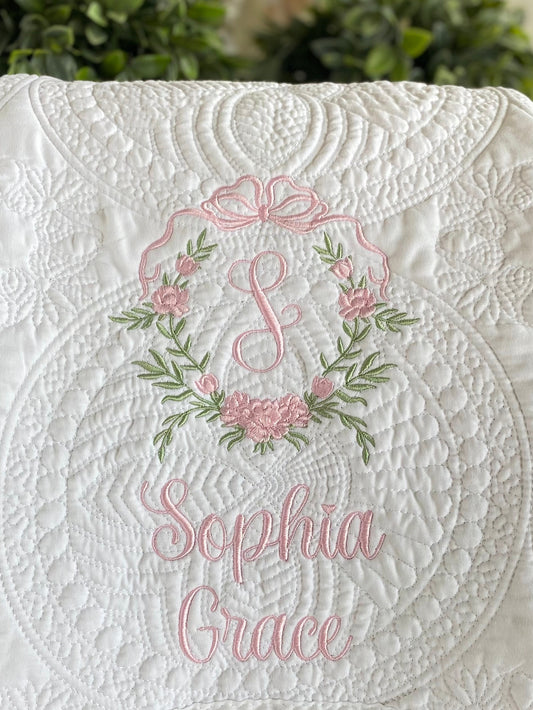 Close-up of a white quilt featuring delicate pink and green embroidery with a floral crest and monogram, personalized with the name Sophia Grace on the Personalized Embroidered Rose Crest Monogram Baby Quilt | Heirloom Keepsake for Girls.
