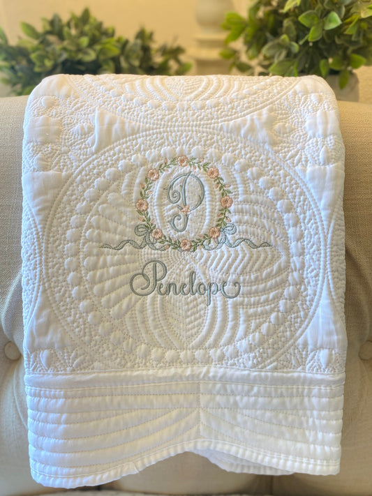 Personalized Embroidered Floral Wreath Monogram Baby Quilt | Heirloom Keepsake featuring delicate floral embroidery and custom monogram with the name Penelope on a soft white quilt.