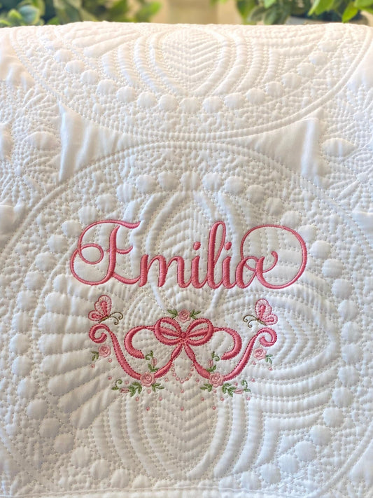 Personalized Embroidered Rose & Butterfly Bow Baby Quilt | Heirloom Keepsake featuring delicate pink embroidery with the name Emilio, surrounded by roses and butterflies on a white quilted fabric.