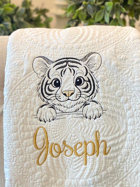 Close-up of a white quilted baby blanket featuring a detailed embroidered tiger cub and the custom name Joseph in gold script, showcasing the Personalized Embroidered Tiger Cub Baby Quilt | Custom Name Heirloom Blanket design.