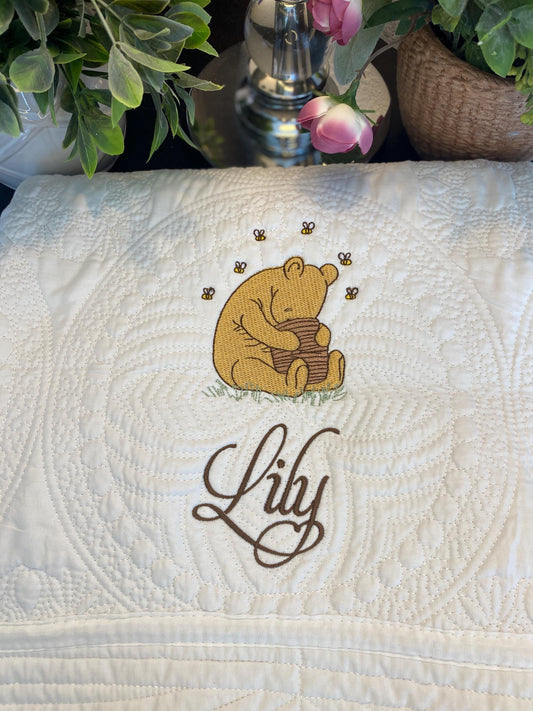 Personalized Storybook Bear Honey Pot Baby Quilt | Custom Name Heirloom Keepsake featuring an embroidered bear holding a honey pot with bees and the name Lily on a quilted white blanket.