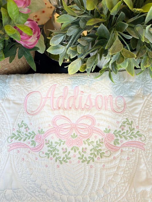 Personalized Embroidered Rose Vine & Bow Baby Quilt | Heirloom Keepsake | Custom Name Blanket featuring delicate pink embroidery of the name Addison with floral vine and bow design on a white quilted background.