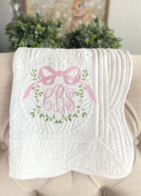 Personalized Vine Bow Crest Monogram Baby Quilt | Custom Embroidered Heirloom Keepsake featuring delicate pink bow, green vine embroidery, and elegant monogram details on a soft white quilt.