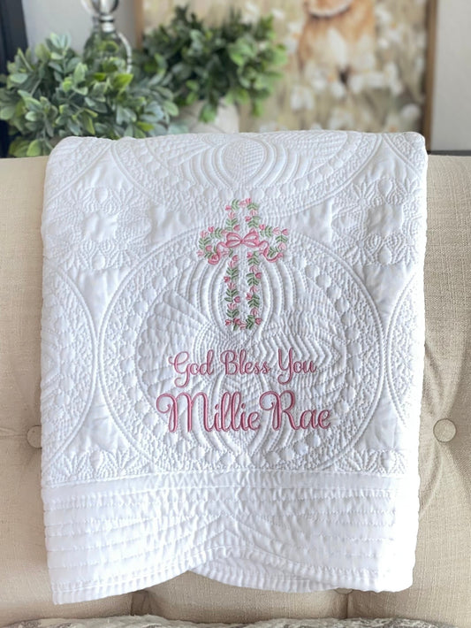White quilt featuring intricate floral vine cross embroidery and personalized "God Bless You Millie Rae" text, showcasing the Personalized God Bless You Floral Vine Cross Baptism Baby Quilt | Christening Heirloom Keepsake.