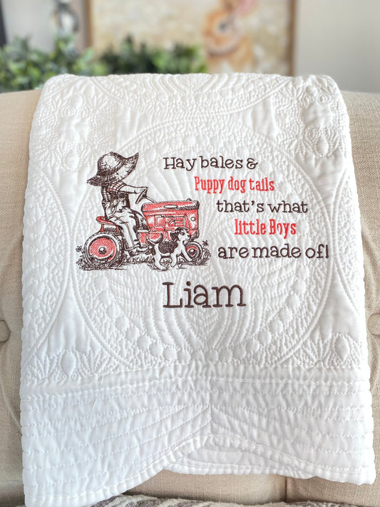 White quilt featuring an embroidered design of a boy on a tractor with a puppy, custom name "Liam," and the phrase "Hay bales & Puppy dog tails that's what little Boys are made of!" on the Personalized Little Tractor Boy & Puppy Baby Quilt | Custom Name Heirloom Blanket for Boys.