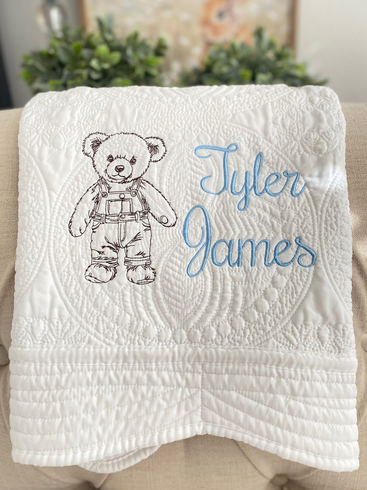 Personalized Embroidered Teddy Bear in Overalls Baby Quilt | Custom Name Heirloom Blanket featuring a detailed teddy bear in overalls and the name Tyler James embroidered in light blue on a white quilted background.