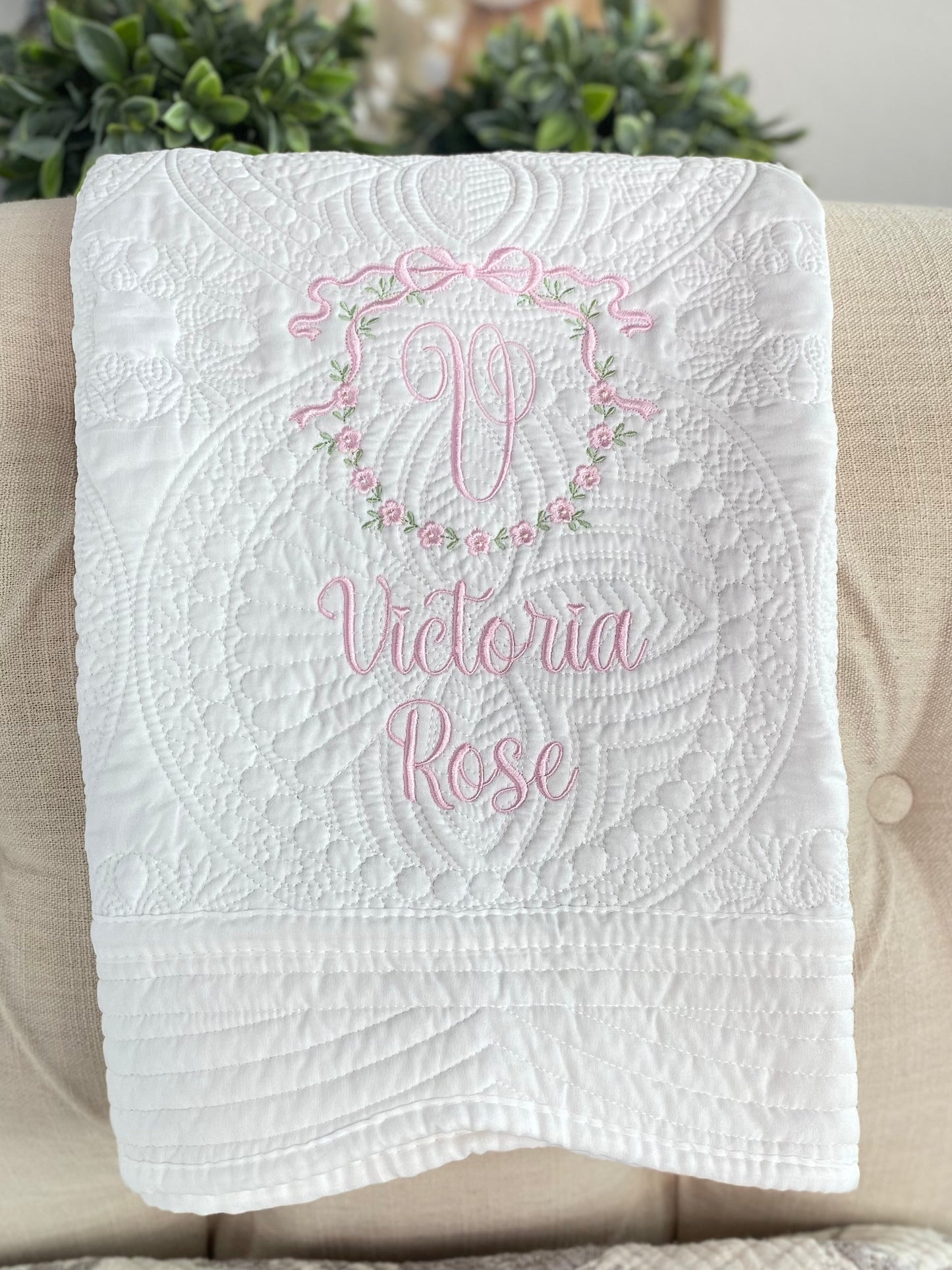 Personalized Bow & Floral Wreath Monogram Baby Quilt | Custom Name Heirloom Keepsake for Girls featuring delicate pink embroidery with a monogram and floral wreath on a white quilted background.