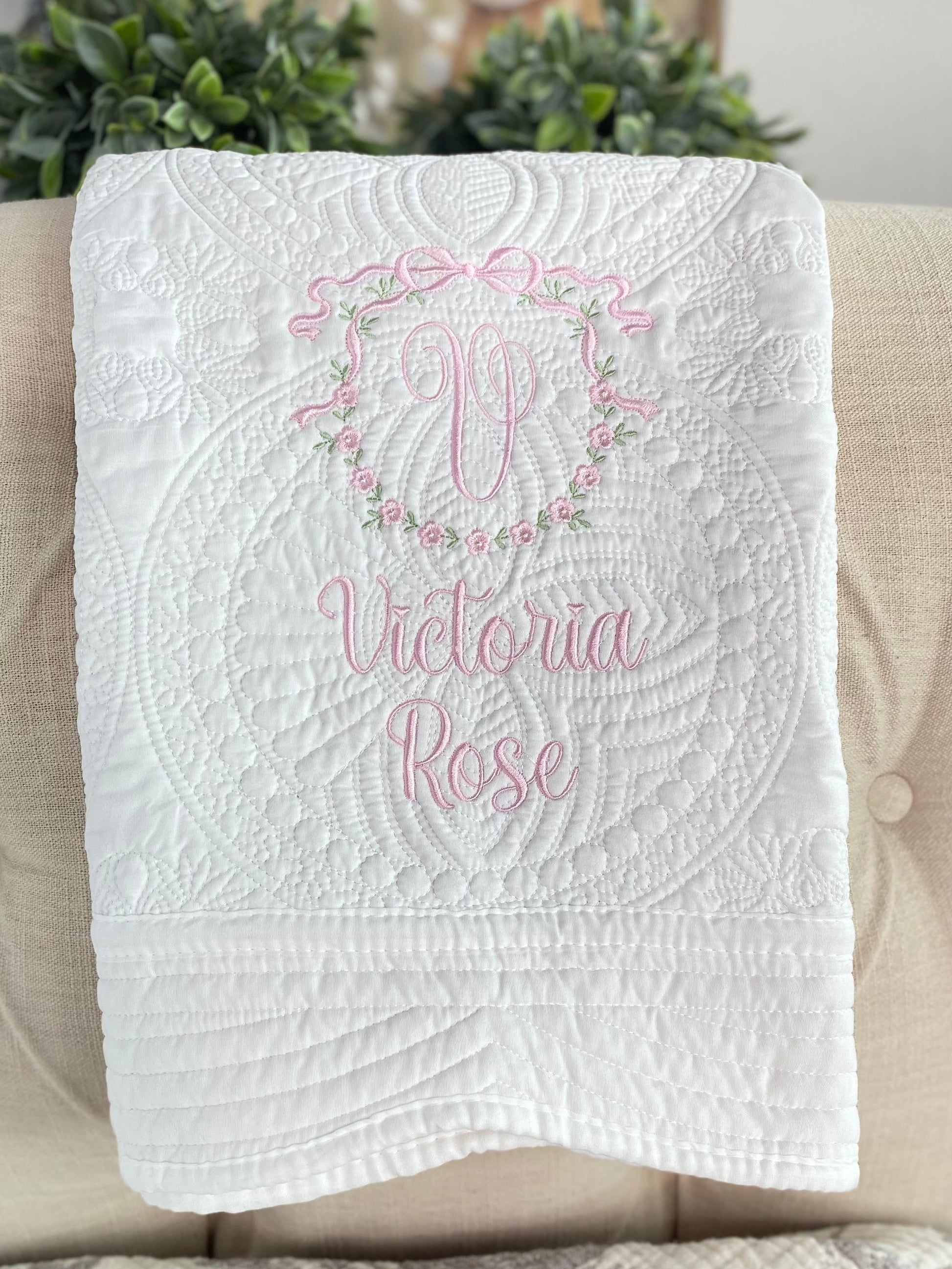 Personalized Bow & Floral Wreath Monogram Baby Quilt | Custom Name Heirloom Keepsake for Girls featuring delicate pink embroidery with a monogram and floral wreath on a white quilted background.