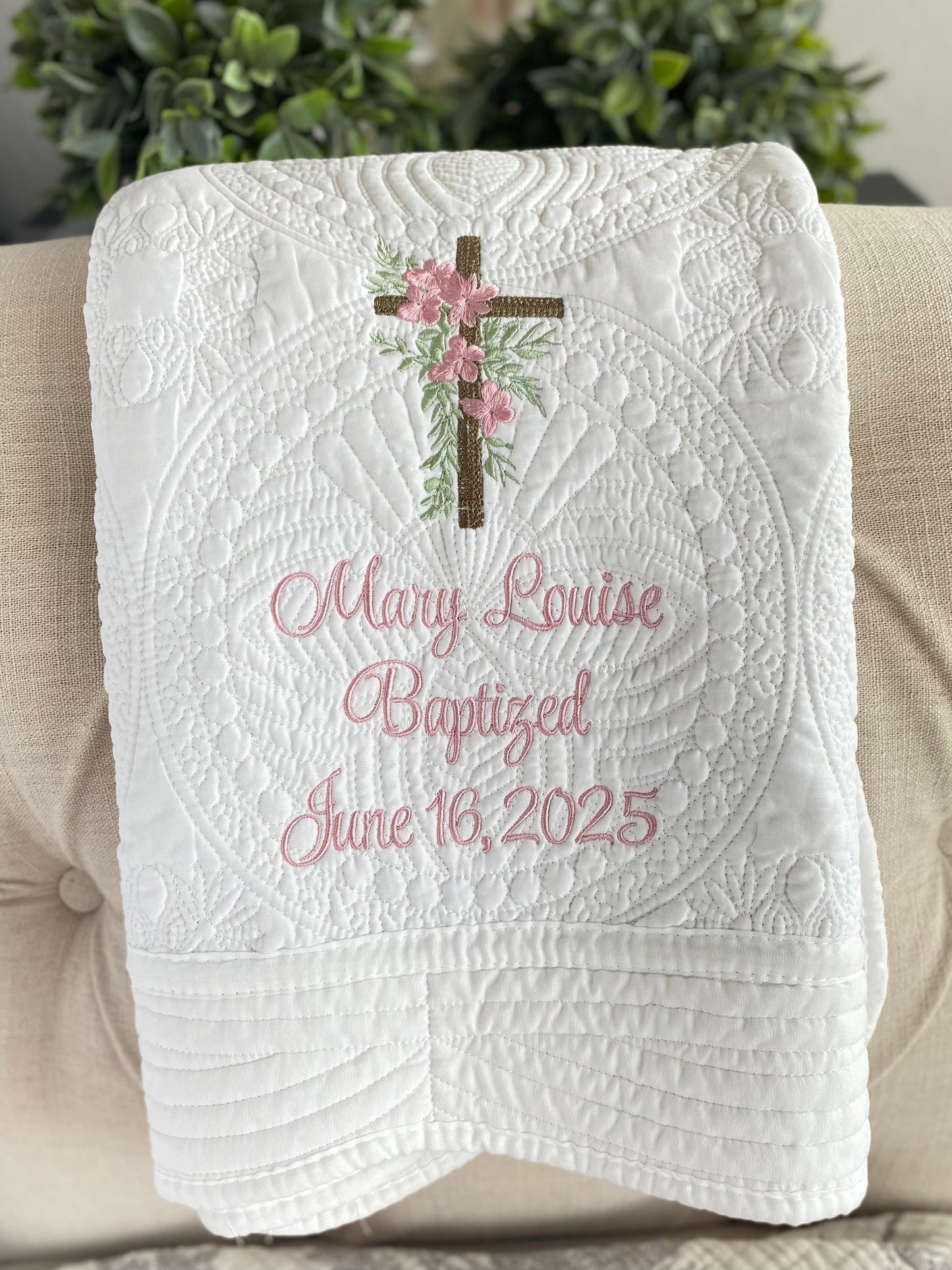 White quilt featuring a personalized rustic cross pink floral baptism baby quilt | custom name & date christening heirloom blanket with delicate embroidery of a cross adorned with pink flowers and green leaves, and soft pink cursive text reading Mary Louise Baptized June 16, 2025.