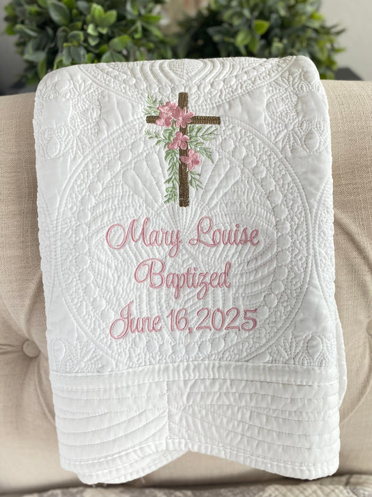 White quilt featuring a personalized rustic cross pink floral baptism baby quilt | custom name & date christening heirloom blanket with delicate embroidery of a cross adorned with pink flowers and green leaves, and soft pink cursive text reading Mary Louise Baptized June 16, 2025.