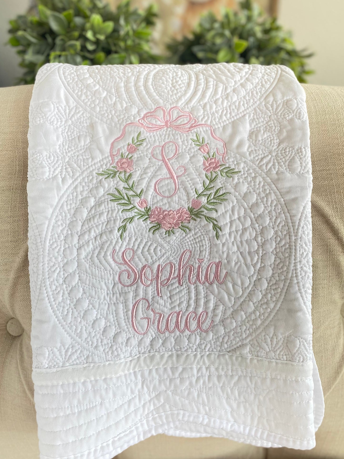 White quilt featuring intricate quilting and a personalized pink embroidered rose crest monogram with the name Sophia Grace, for the Personalized Embroidered Rose Crest Monogram Baby Quilt | Heirloom Keepsake for Girls.