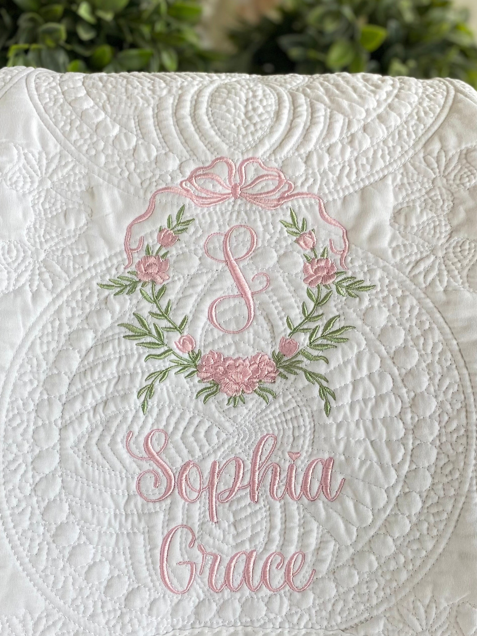 Close-up of a white quilt featuring delicate pink and green embroidery with a floral crest and monogram, personalized with the name Sophia Grace on the Personalized Embroidered Rose Crest Monogram Baby Quilt | Heirloom Keepsake for Girls.