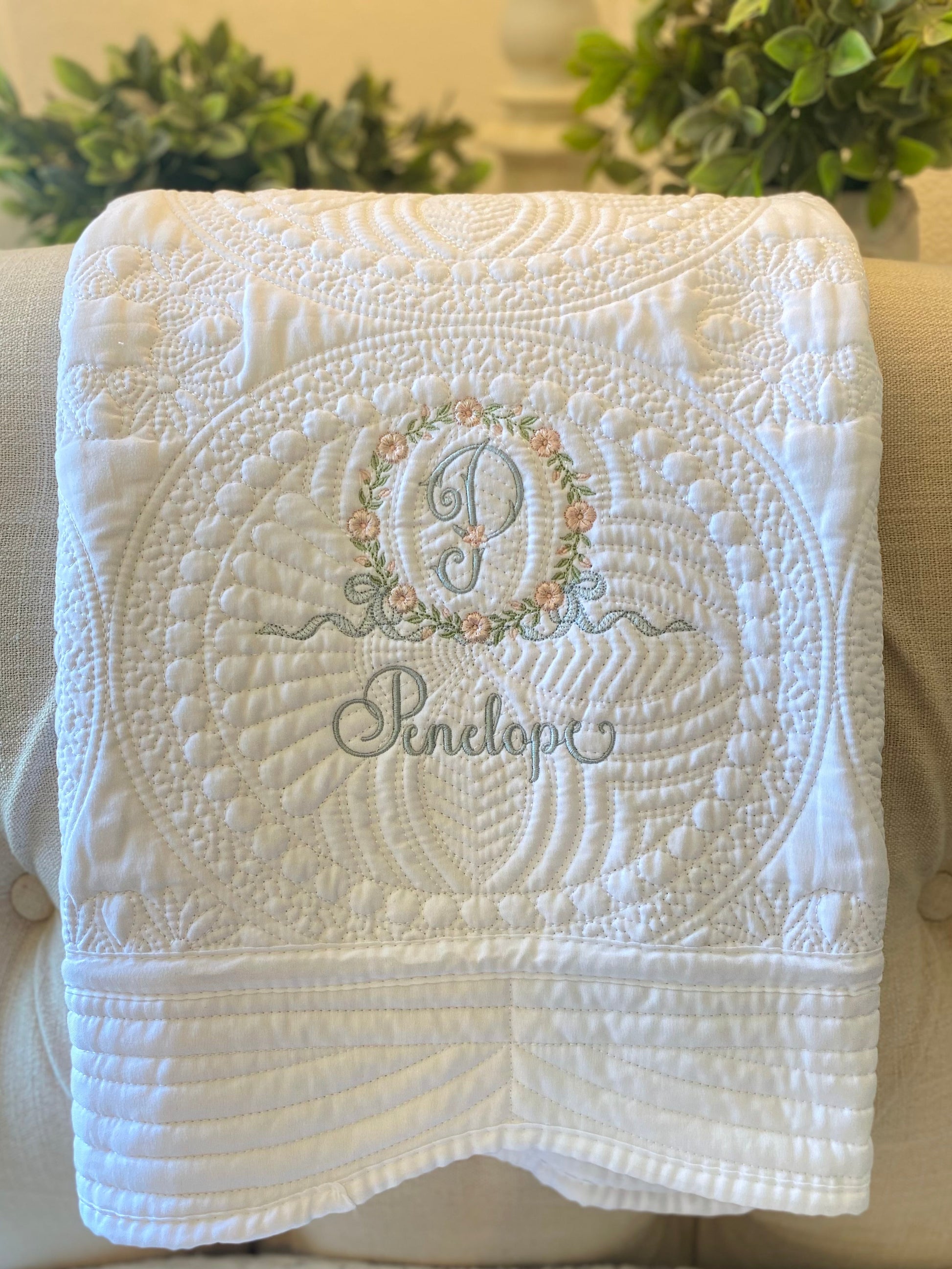 Personalized Embroidered Floral Wreath Monogram Baby Quilt | Heirloom Keepsake featuring delicate floral embroidery and custom monogram with the name Penelope on a soft white quilt.