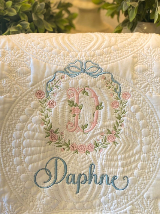 Close-up of a Personalized Embroidered Bow & Floral Wreath Monogram Baby Quilt | Heirloom Keepsake featuring delicate floral embroidery, soft pastel colors, and a custom name in elegant script.