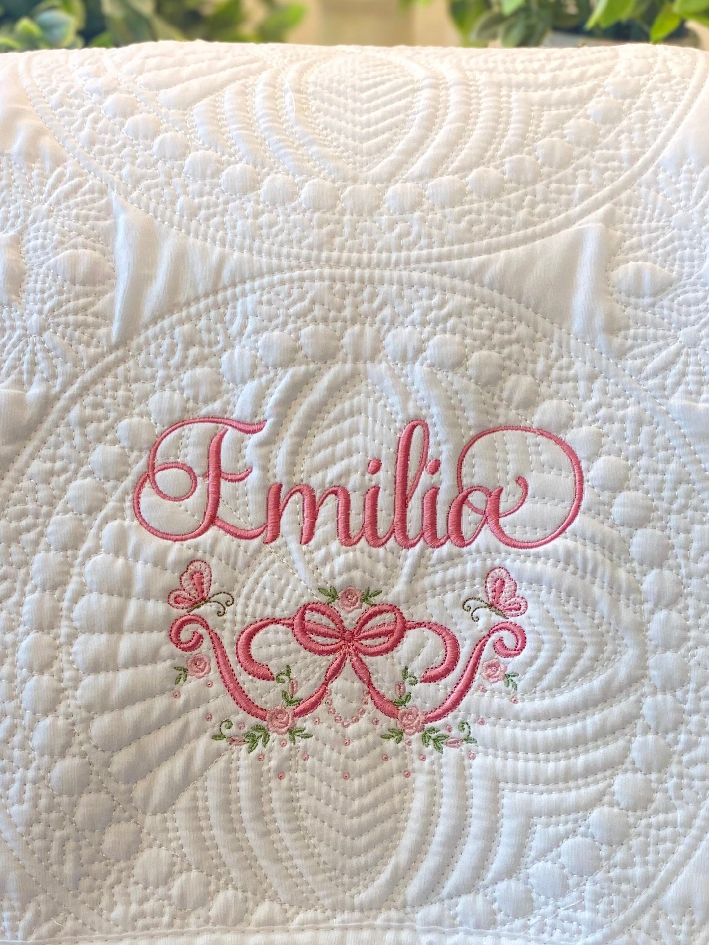 Personalized Embroidered Rose & Butterfly Bow Baby Quilt | Heirloom Keepsake featuring delicate pink embroidery with the name Emilio, surrounded by roses and butterflies on a white quilted fabric.