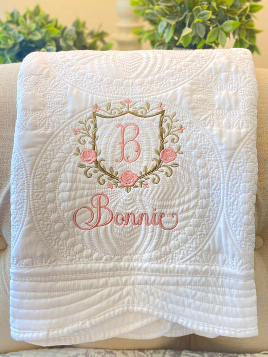 Personalized Embroidered Rose Crest Monogram Baby Quilt | Heirloom Keepsake featuring delicate pink and green embroidery of roses and monogram "B" with the name Bonnie on a white quilted background.