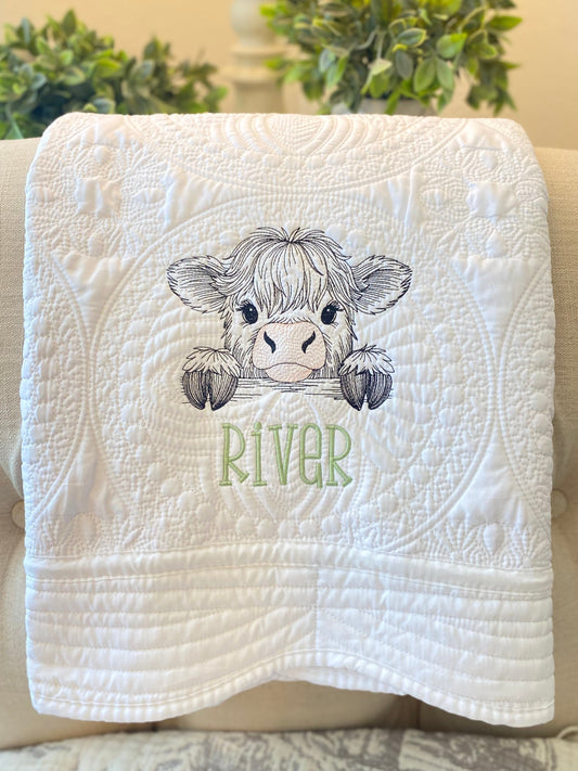 White quilt with intricate stitching featuring an embroidered peeking Highland cow and the name River in green, showcasing the Personalized Embroidered Peeking Highland Cow Baby Quilt | Custom Name Heirloom Blanket.