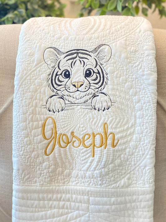 Personalized Embroidered Tiger Cub Baby Quilt | Custom Name Heirloom Blanket with a detailed embroidered tiger cub and the custom name Joseph in golden thread on a white textured quilt.
