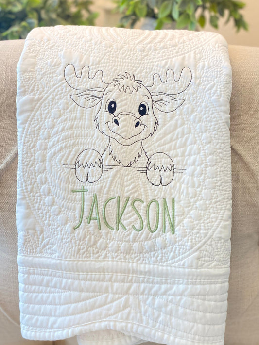 White quilt featuring an embroidered moose design and a custom name in green, showcasing the Personalized Embroidered Moose Baby Quilt | Custom Name Heirloom Blanket as a handmade heirloom baby gift.
