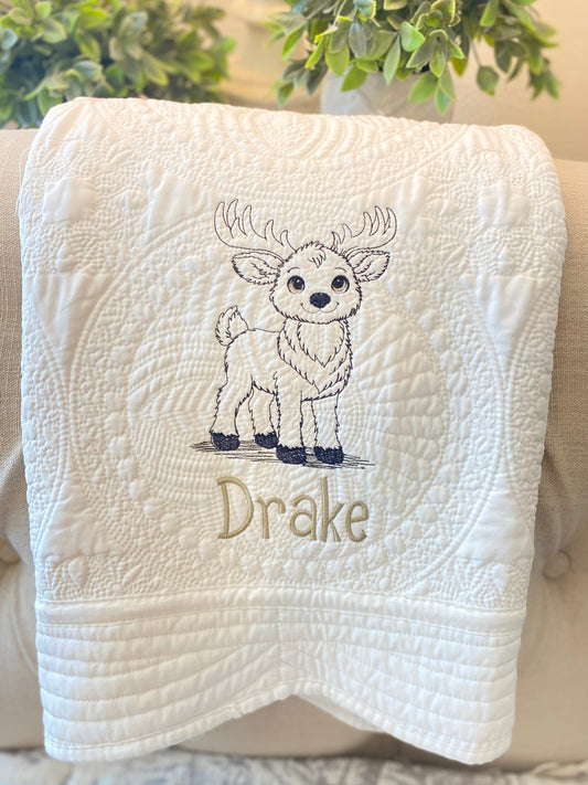 White embroidered baby quilt featuring a detailed reindeer design and the name Drake, showcasing the Personalized Embroidered Reindeer Baby Quilt | Custom Name Heirloom Blanket perfect for a newborn gift.