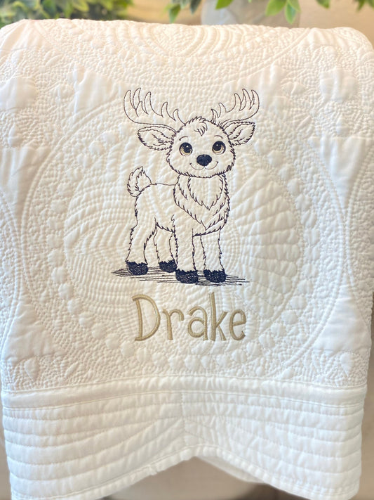 Personalized Embroidered Reindeer Baby Quilt | Custom Name Heirloom Blanket featuring a detailed embroidered reindeer design with the name Drake on a soft, white quilt.