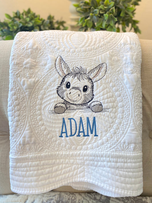 White quilt with intricate quilting details featuring a personalized embroidered donkey and the name Adam, showcasing the Personalized Embroidered Donkey Baby Quilt | Custom Name Heirloom Blanket.
