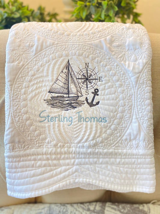 Personalized Embroidered Sailboat Compass & Anchor Baby Quilt | Custom Name Heirloom Blanket featuring a detailed sailboat, compass, and anchor embroidery with a custom name on a white quilted fabric.