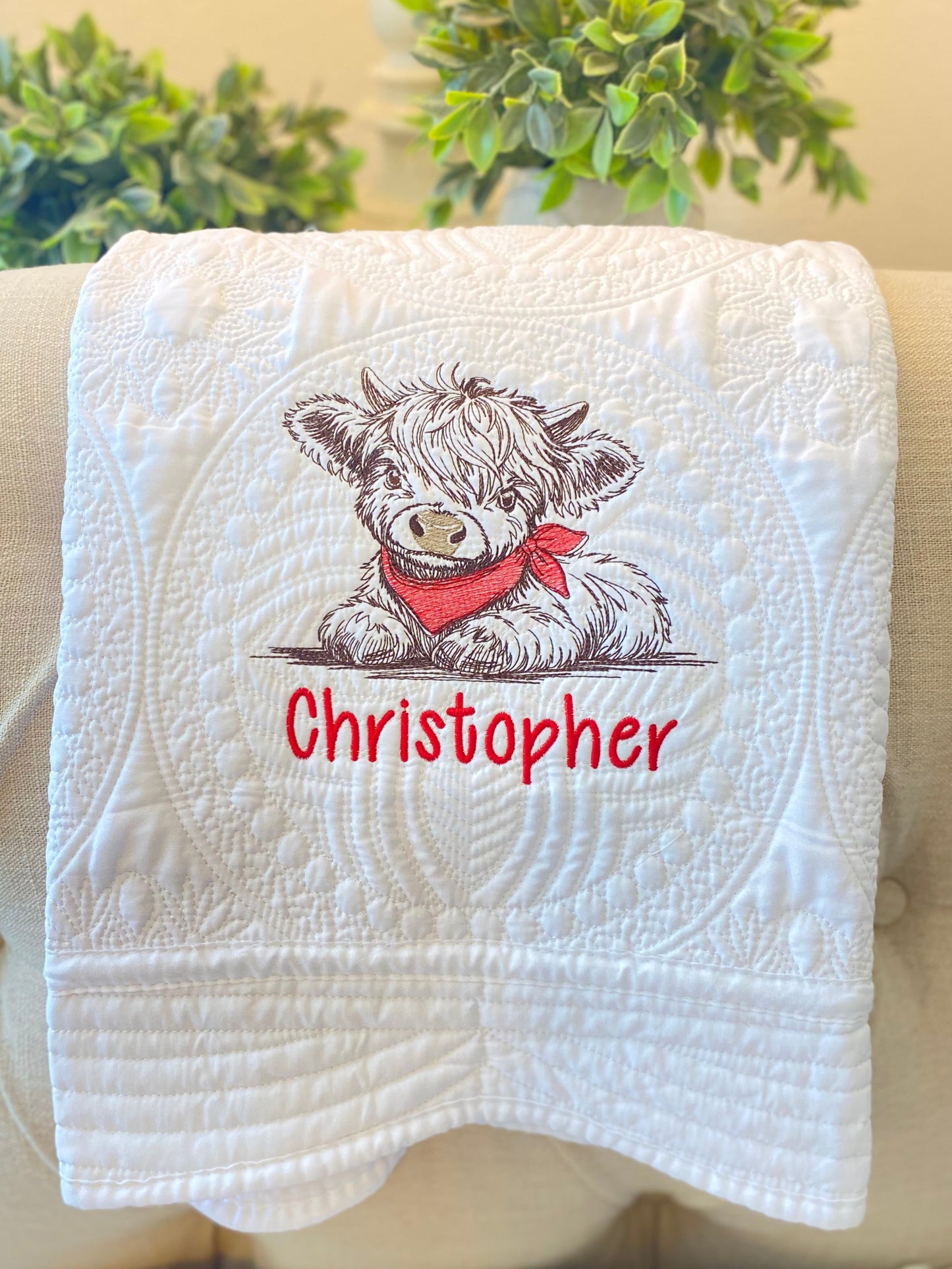 Personalized Embroidered Highland Cow Baby Quilt | Custom Name Heirloom Blanket featuring a detailed embroidered highland cow with a red scarf and the name Christopher on a white quilted background, perfect as a personalized baby quilt or heirloom baby gift.