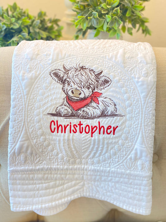Personalized Embroidered Highland Cow Baby Quilt | Custom Name Heirloom Blanket featuring a detailed embroidered highland cow with a red scarf and the name Christopher on a white quilted background, perfect as a personalized baby quilt or heirloom baby gift.