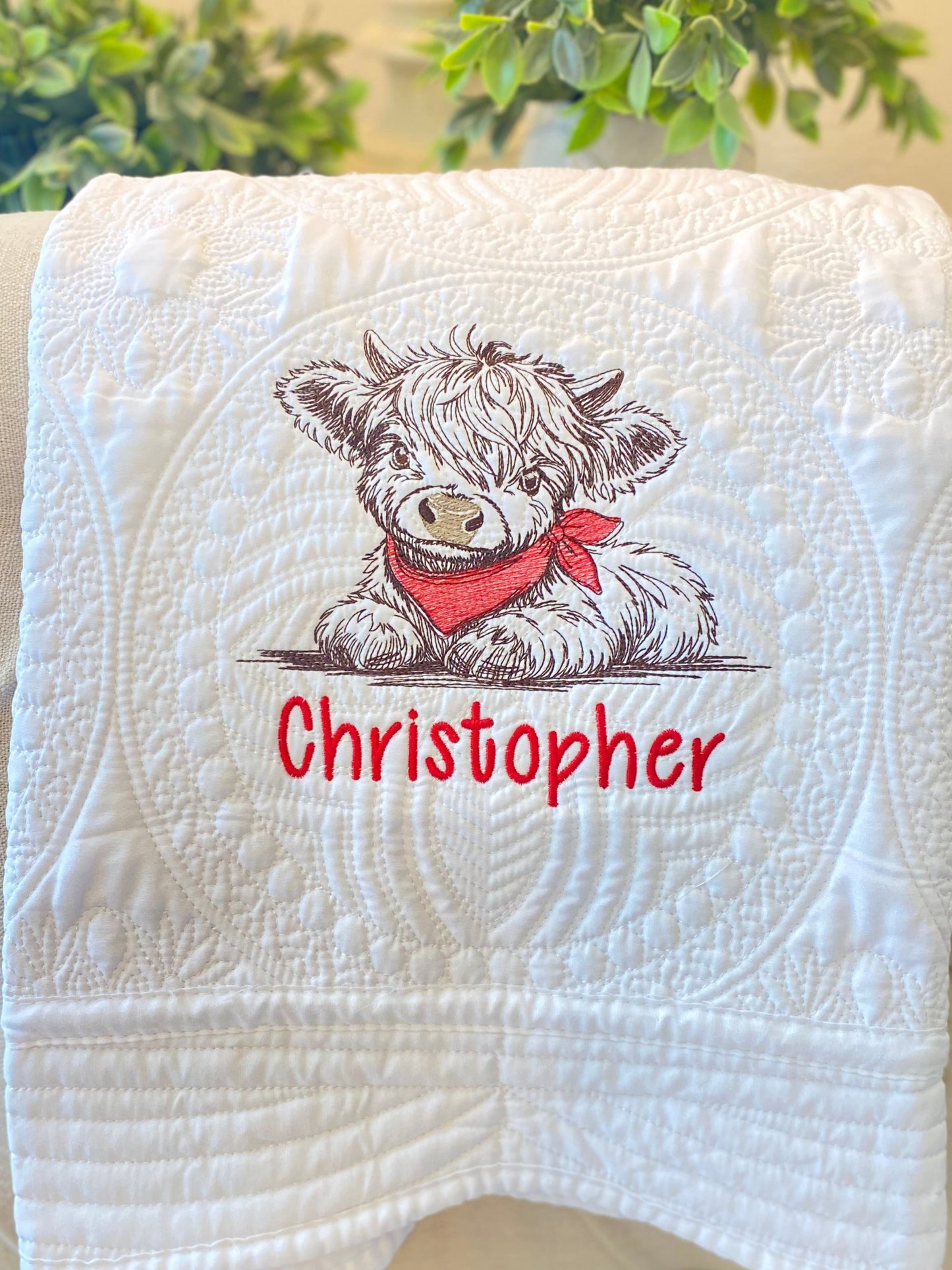 White quilt featuring detailed embroidery of a Highland cow wearing a red bandana above the personalized name Christopher, showcasing the Personalized Embroidered Highland Cow Baby Quilt | Custom Name Heirloom Blanket design.