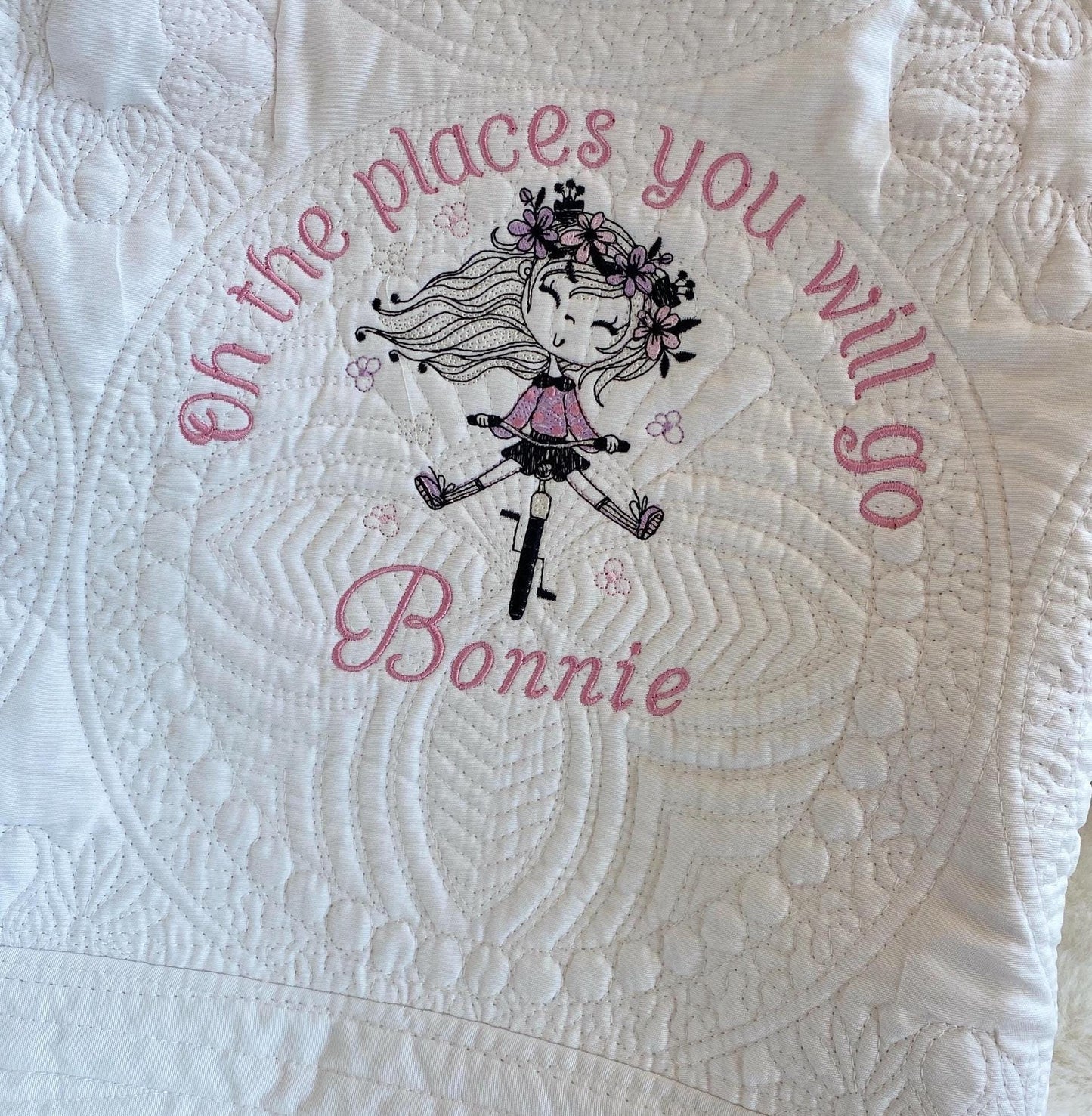 Close-up of a Personalized Embroidered Girl on Bike Baby Quilt | Adventure Heirloom Keepsake | Custom Name Blanket showing detailed stitching, featuring a girl on a bike with floral accents and the phrase "oh the places you will go" along with a custom name.