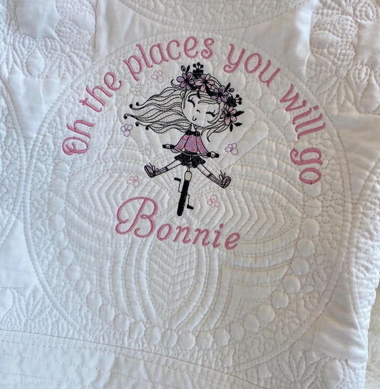 Close-up of a Personalized Embroidered Girl on Bike Baby Quilt | Adventure Heirloom Keepsake | Custom Name Blanket showing detailed stitching, featuring a girl on a bike with floral accents and the phrase "oh the places you will go" along with a custom name.