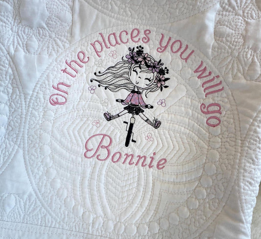 Close-up of a white Personalized Embroidered Girl on Bike Baby Quilt | Adventure Heirloom Keepsake | Custom Name Blanket featuring a stitched design of a girl on a bike with flowers and the phrase "Oh the places you will go" along with the custom name Bonnie.