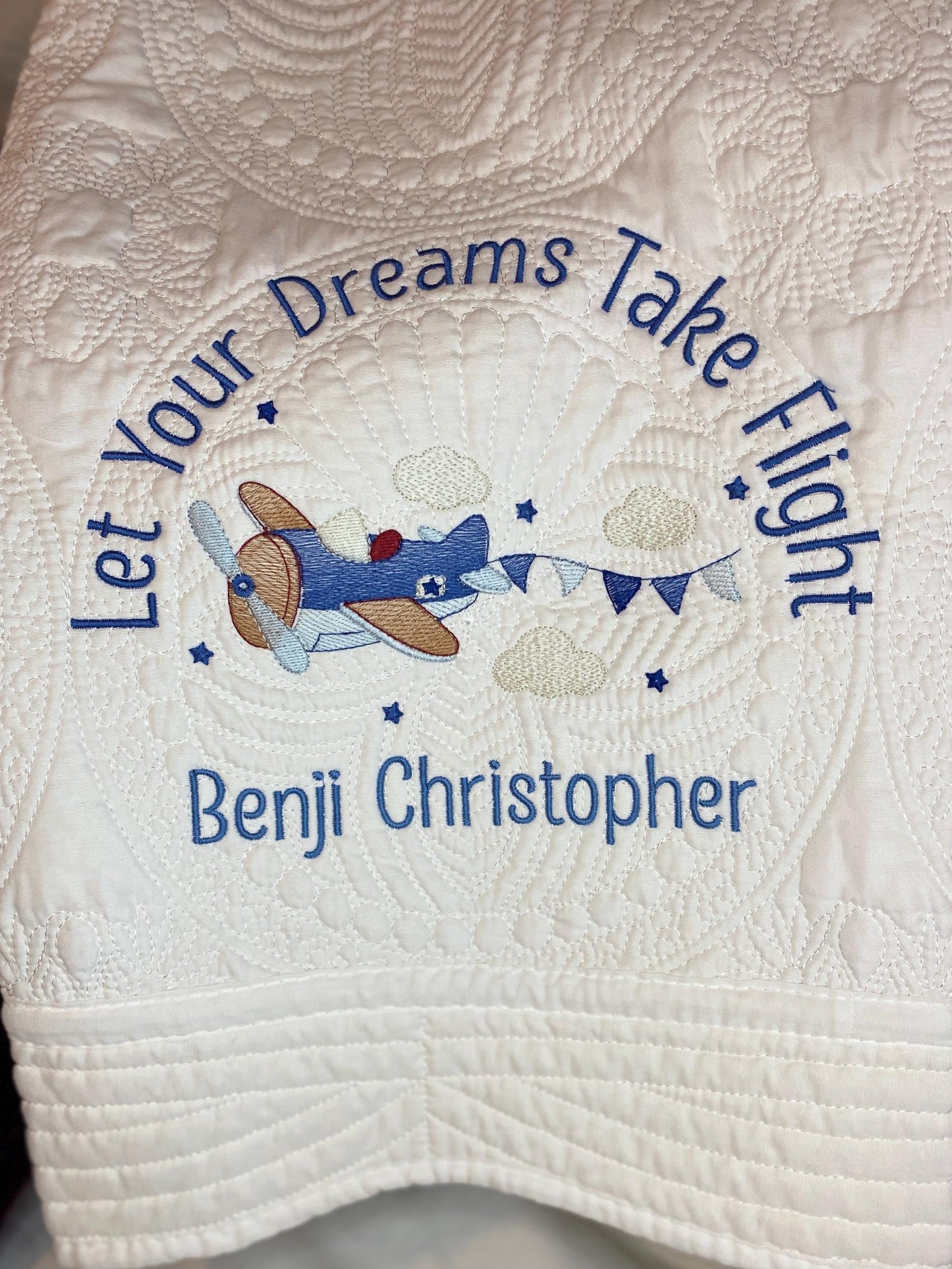Personalized "Let Your Dreams Take Flight" Airplane Baby Quilt | Custom Name Blanket | Heirloom Keepsake featuring embroidered vintage airplane with clouds and custom name Benji Christopher on a white quilted background.