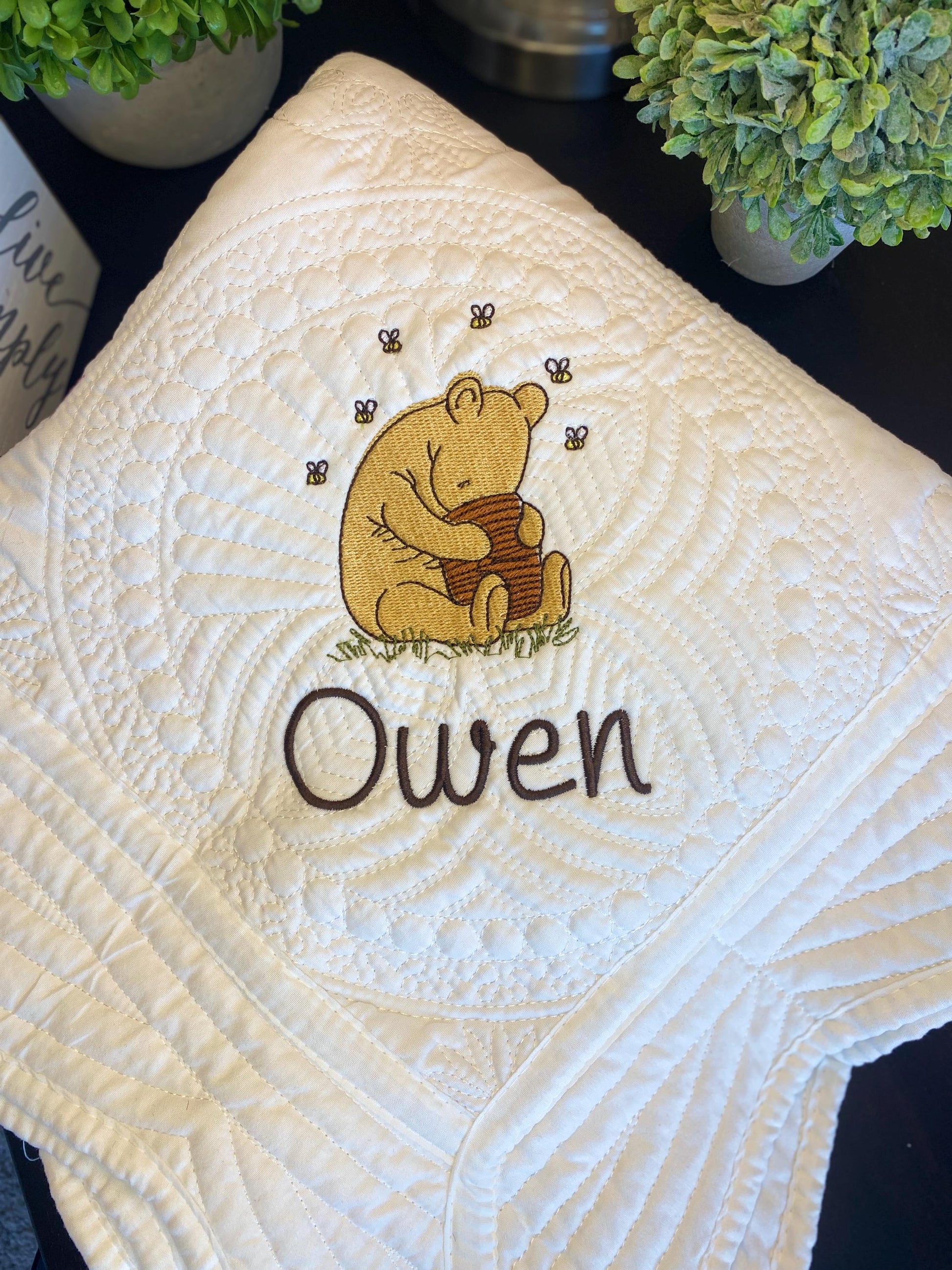 Personalized Storybook Bear Honey Pot Baby Quilt | Custom Name Heirloom Keepsake with embroidered bear hugging honey pot and custom name Owen on a white quilted baby blanket.