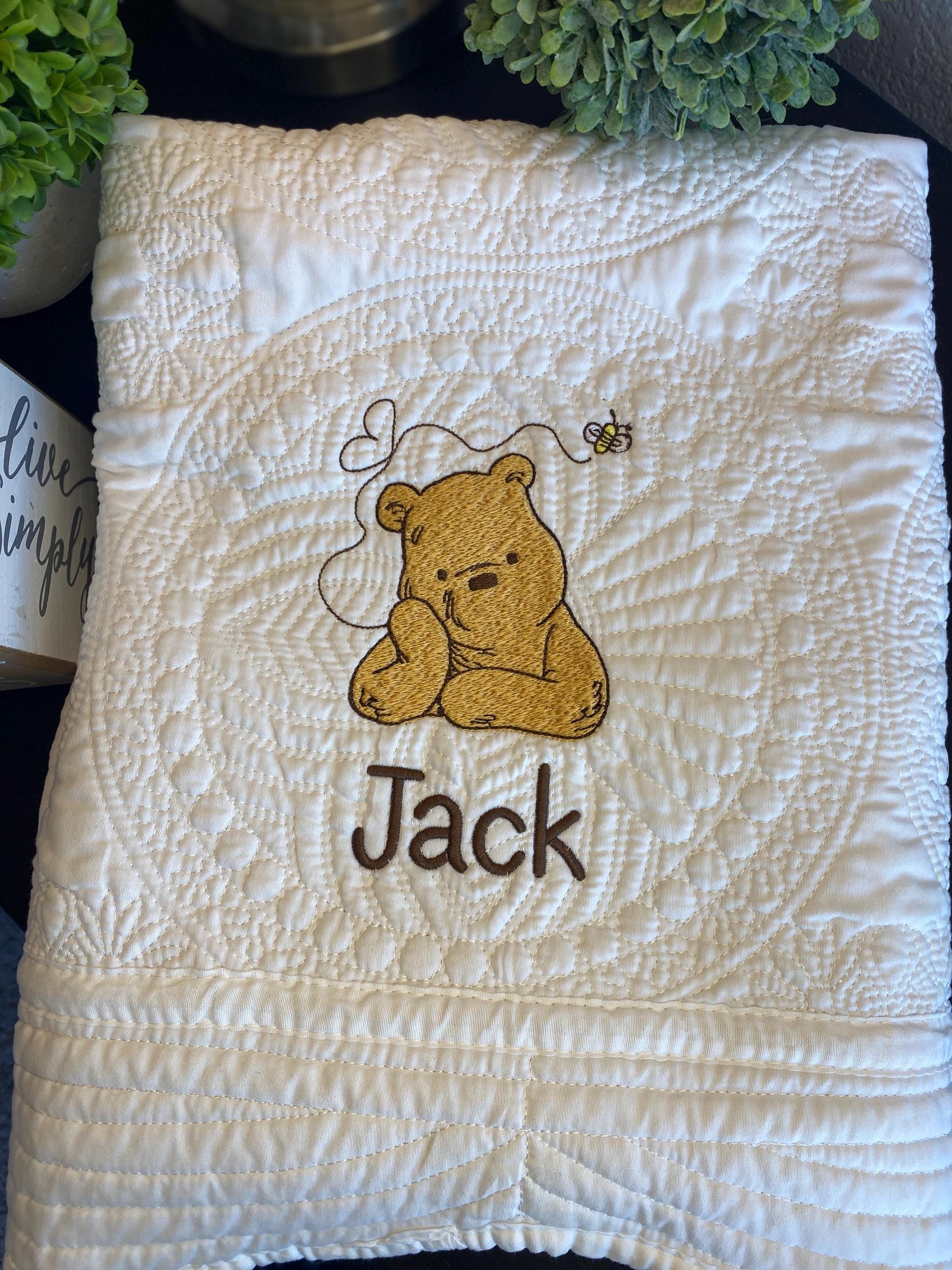 Personalized Storybook Bear Honey Bee Baby Quilt | Custom Name Heirloom Keepsake featuring a quilted white blanket with an embroidered bear, honey bee, and custom name "Jack" in brown thread.