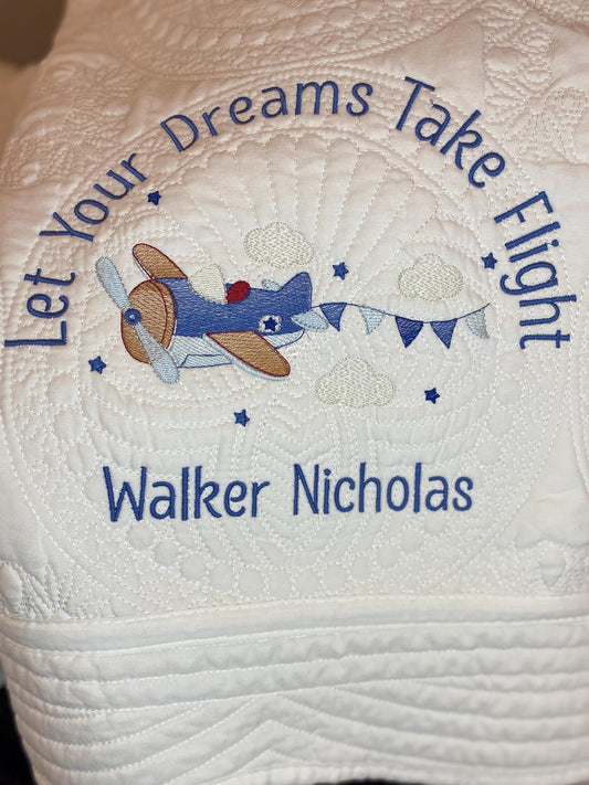 Personalized "Let Your Dreams Take Flight" Airplane Baby Quilt | Custom Name Blanket | Heirloom Keepsake featuring a blue embroidered airplane with clouds and stars on a white quilted background.