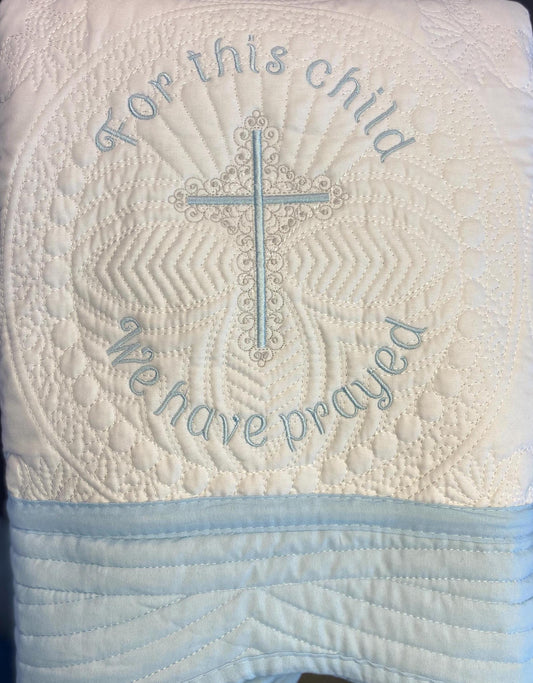 For This Child We Have Prayed" Cross Baby Quilt | Custom Embroidered Baptism Heirloom Blanket featuring intricate quilting with a blue embroidered cross and prayer message on a soft white fabric background.