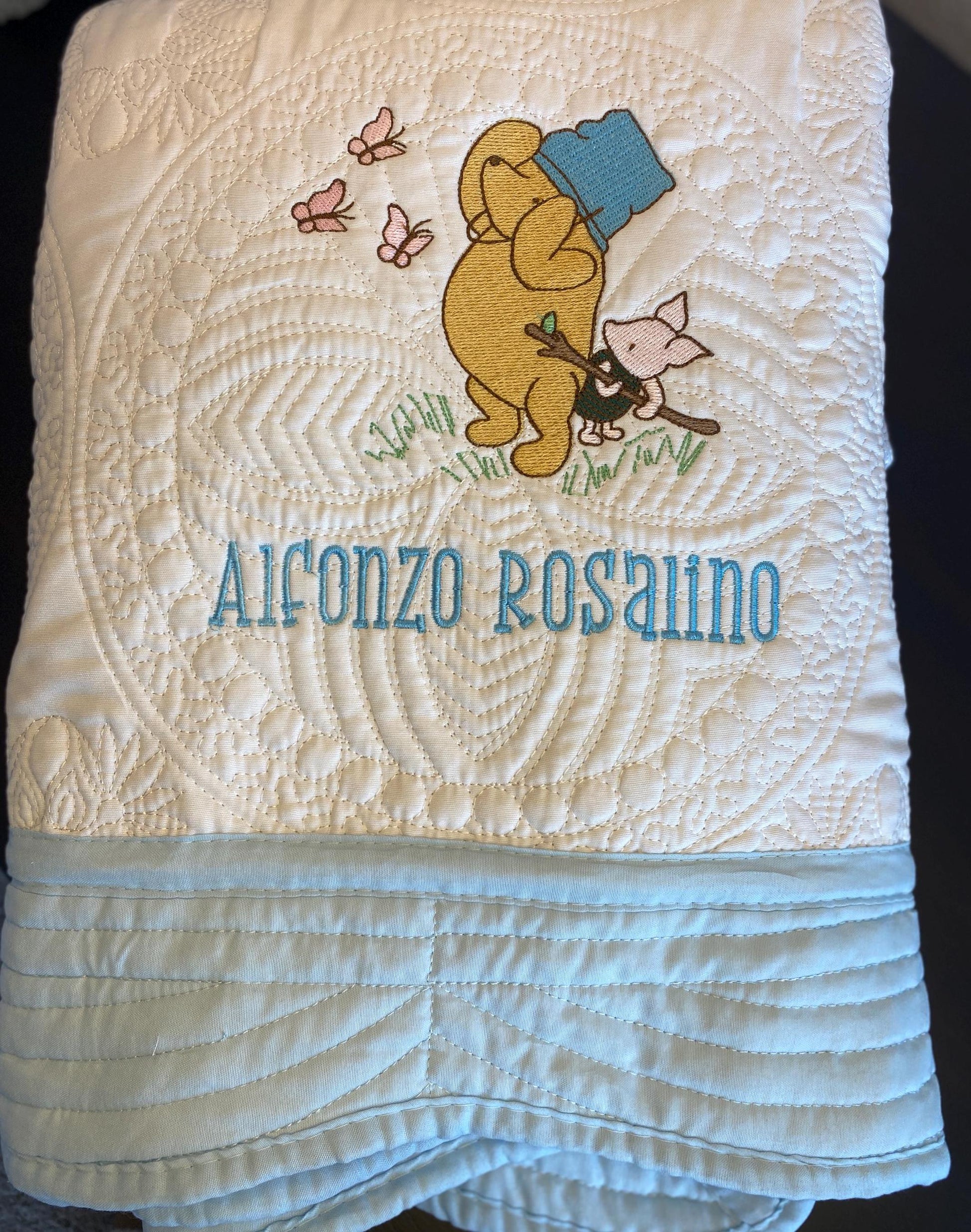Personalized Storybook Bear & Friend with Bees Baby Quilt | Custom Name Heirloom Keepsake showing a cozy quilt with embroidered bear in a blue hat, small friend, bees, and custom name "Alfonzo Rosalino" in blue thread.
