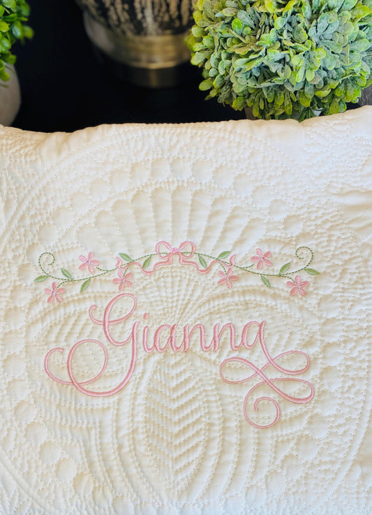 Close-up of an elegant white quilt with intricate stitching, personalized with the name Gianna in pink script, adorned with delicate floral vine and bow embroidery, showcasing the Personalized Floral Vine & Bow Baby Quilt | Custom Name Heirloom Keepsake.