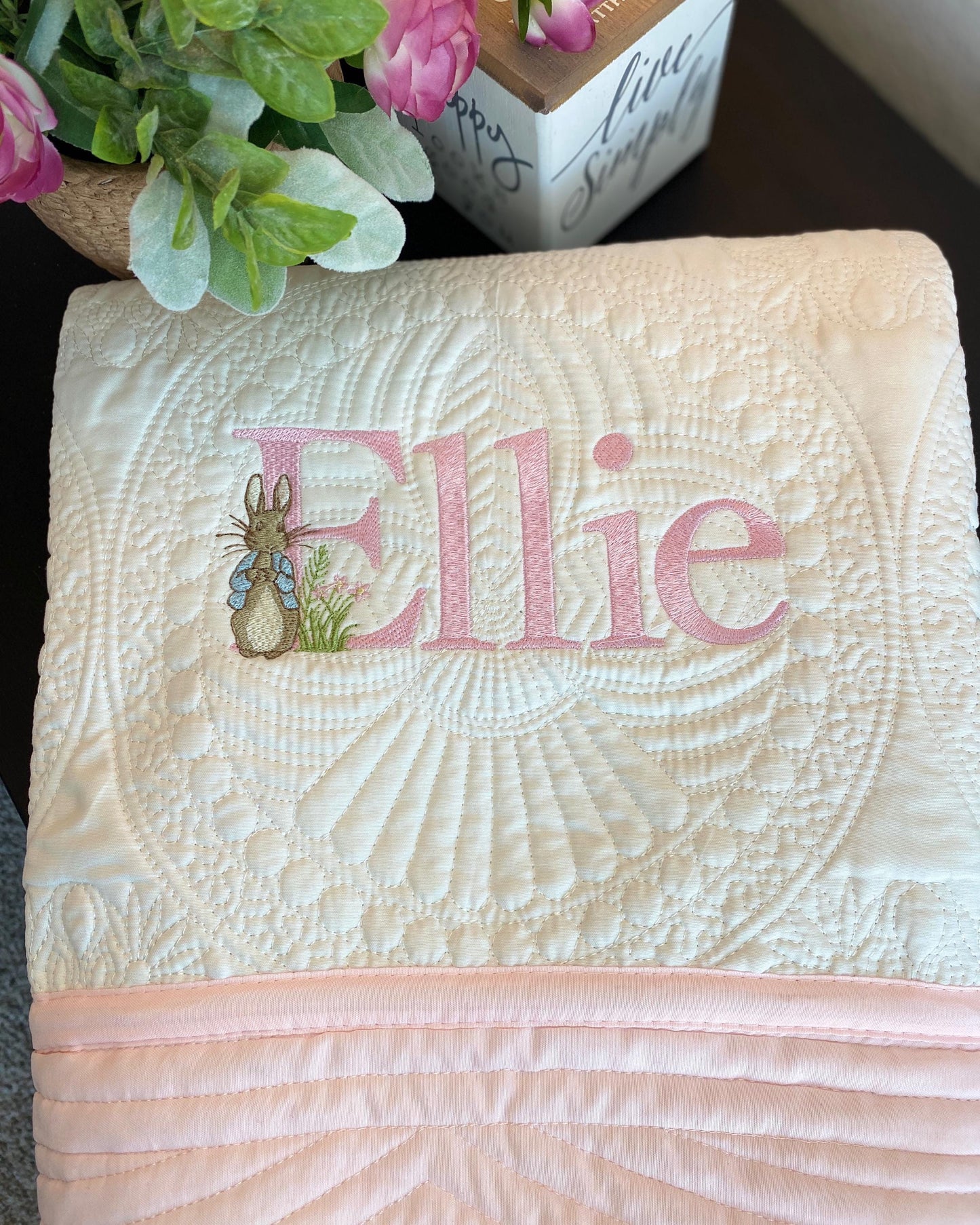 Folded Personalized Classic Storybook Bunny Baby Quilt | Custom Name Heirloom Blanket with the name Ellie embroidered in pink script alongside a small bunny design, featuring intricate quilted detailing.
