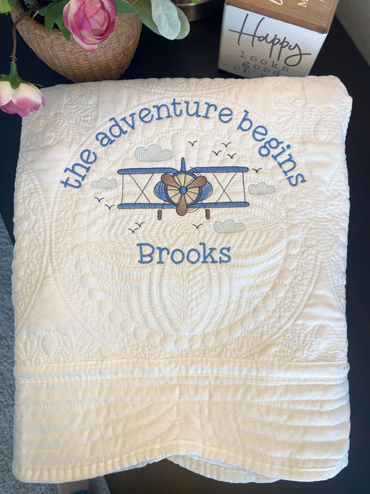 Personalized Vintage Airplane Quilt | Custom Name Heirloom Blanket featuring an embroidered vintage airplane and the phrase "the adventure begins" with the name Brooks on a soft, white quilted fabric.