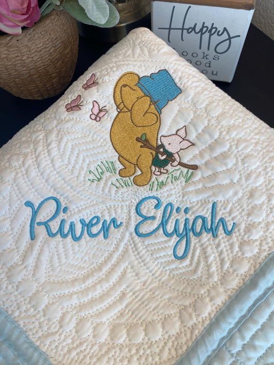 Personalized Storybook Bear & Friend with Bees Baby Quilt | Custom Name Heirloom Keepsake featuring embroidered bear, friend, and butterflies with custom name River Elijah on a quilted soft cream background.