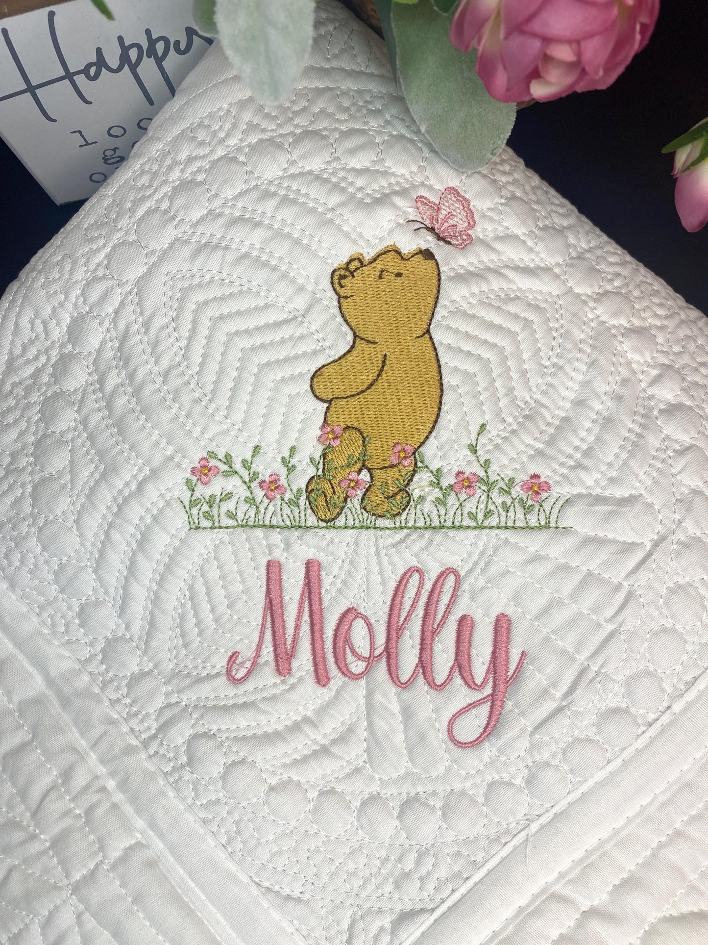 Personalized Storybook Bear & Butterfly Baby Quilt | Custom Name Heirloom Keepsake featuring an embroidered bear looking at a butterfly above pink flowers with the name Molly in pink script on a white quilted background.
