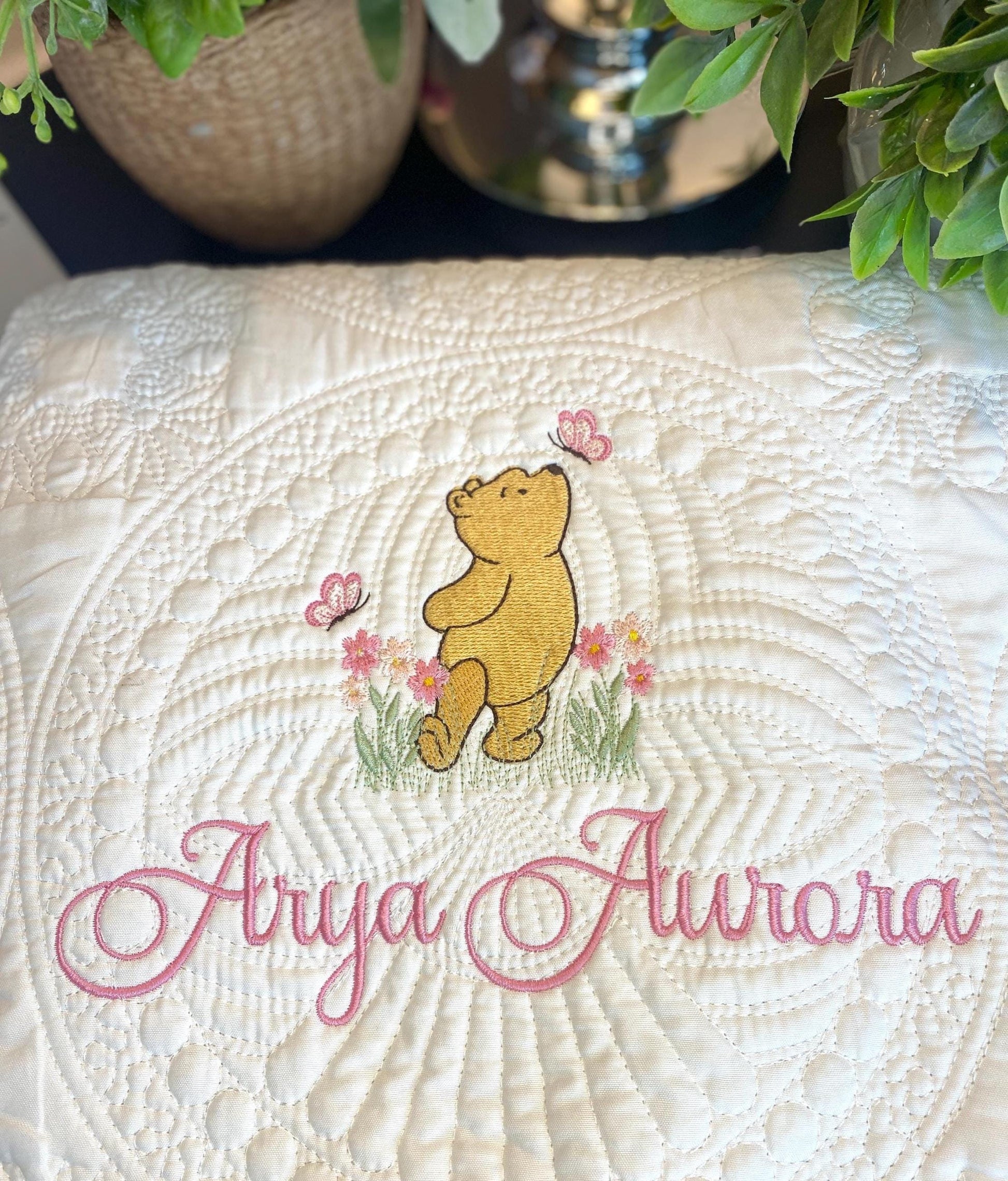 Embroidered bear with pink flowers and butterflies on a cream quilt featuring custom name embroidery, showcasing the Personalized Storybook Bear Pink Flowers & Butterflies Baby Quilt | Custom Name Heirloom Keepsake.