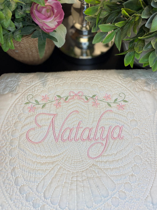 Personalized Floral Vine & Bow Baby Quilt | Custom Name Heirloom Keepsake featuring delicate pink embroidery with the name Natalya surrounded by floral vine and bow design on a soft white quilt.