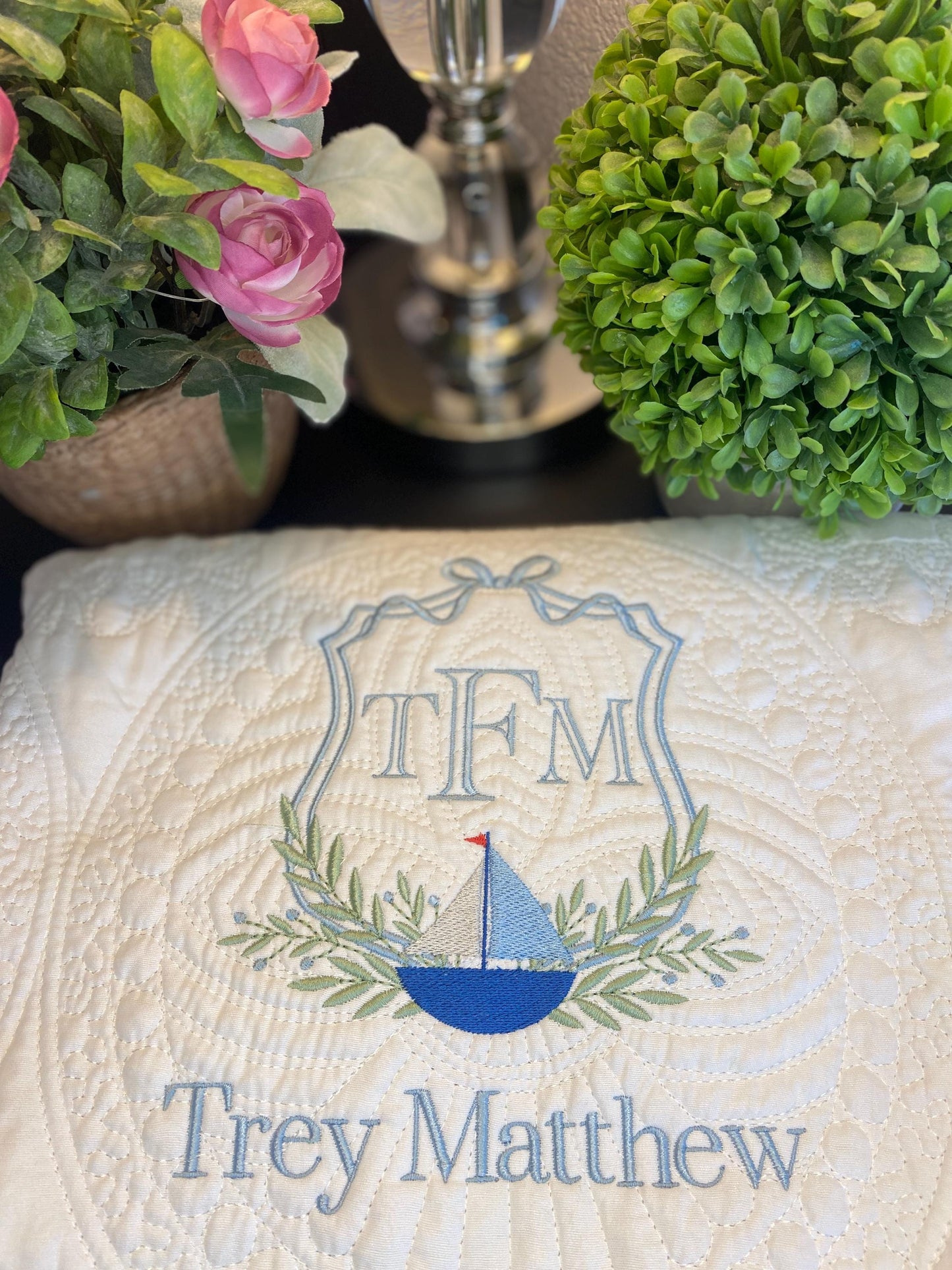 Personalized Sailboat Crest Monogram Baby Quilt | Custom Embroidered Heirloom Blanket for Boys with blue sailboat, green leaves, and name Trey Matthew stitched on white quilt.
