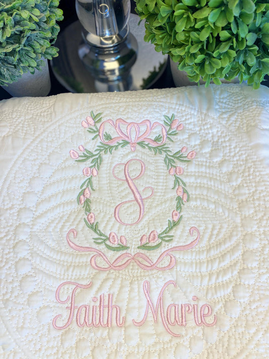 Personalized Secret Garden Floral Wreath Monogram Baby Quilt | Custom Embroidered Heirloom Blanket with delicate pink floral wreath, monogram S, and name Faith Marie embroidered on soft white fabric.