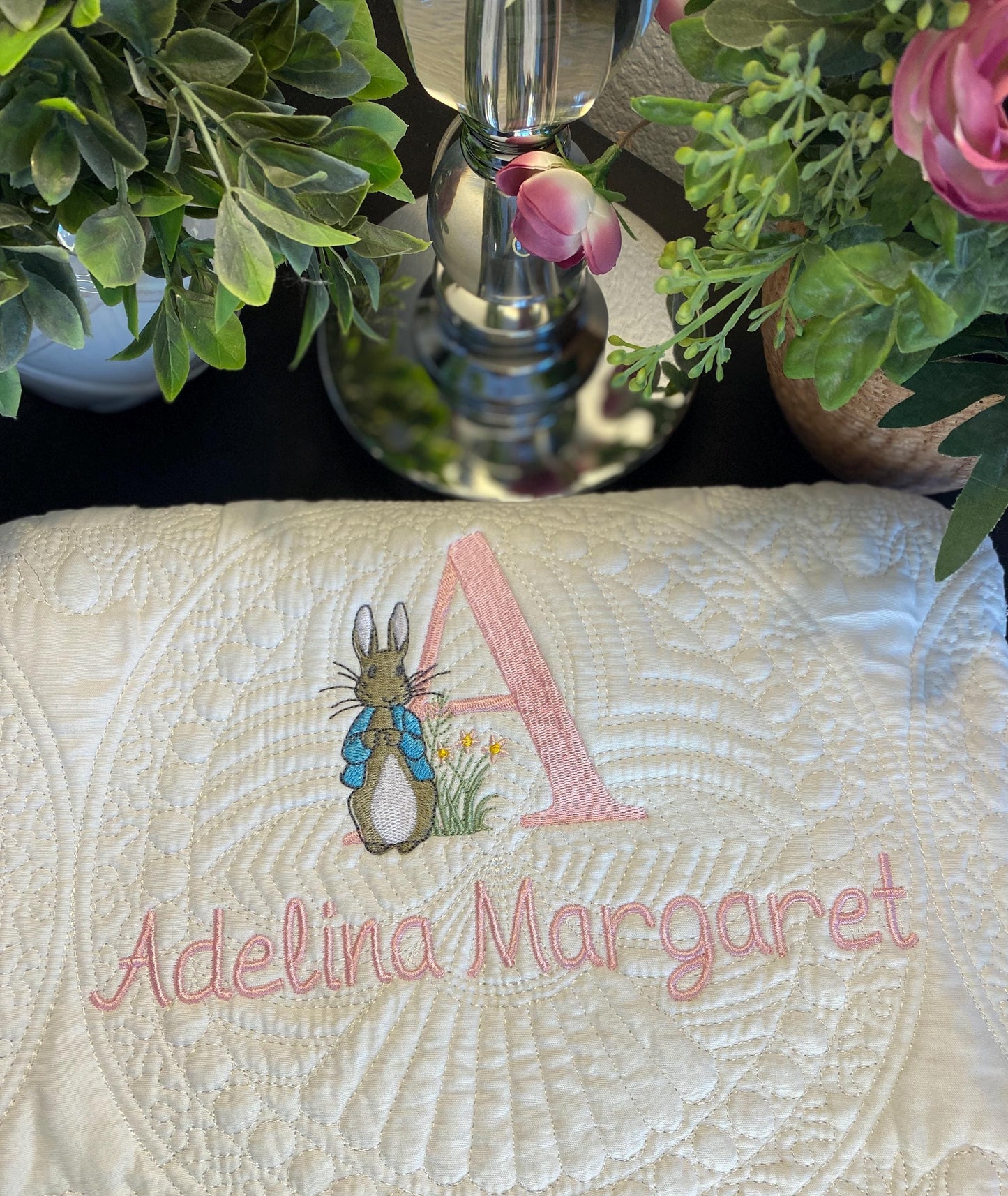 Close-up of a cream-colored personalized embroidered baby quilt with a detailed bunny, pink initial "A," and the name Adelina Margaret stitched in soft pink, styled as the Personalized Embroidered Bunny Baby Quilt | Classic Storybook Heirloom Keepsake | Custom Name Blanket.