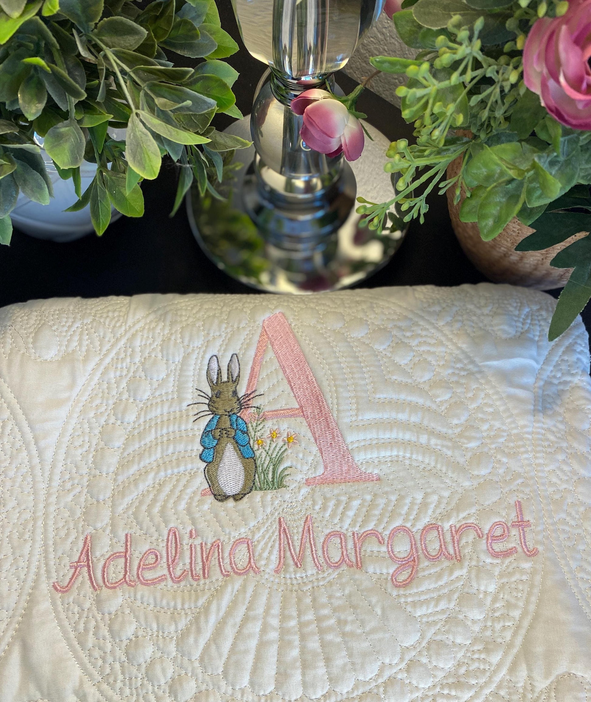 Close-up of a cream-colored personalized embroidered baby quilt with a detailed bunny, pink initial "A," and the name Adelina Margaret stitched in soft pink, styled as the Personalized Embroidered Bunny Baby Quilt | Classic Storybook Heirloom Keepsake | Custom Name Blanket.